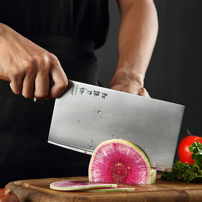 Person cutting a watermelon with a large knife on a wooden cutting board.